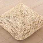 Coussin carré en rotin clair sur un fond beige.