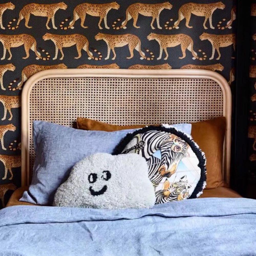 Tête de lit en rotin sur un mur léopard. Le lit possède des draps bleus et des coussins sont posés dessus.