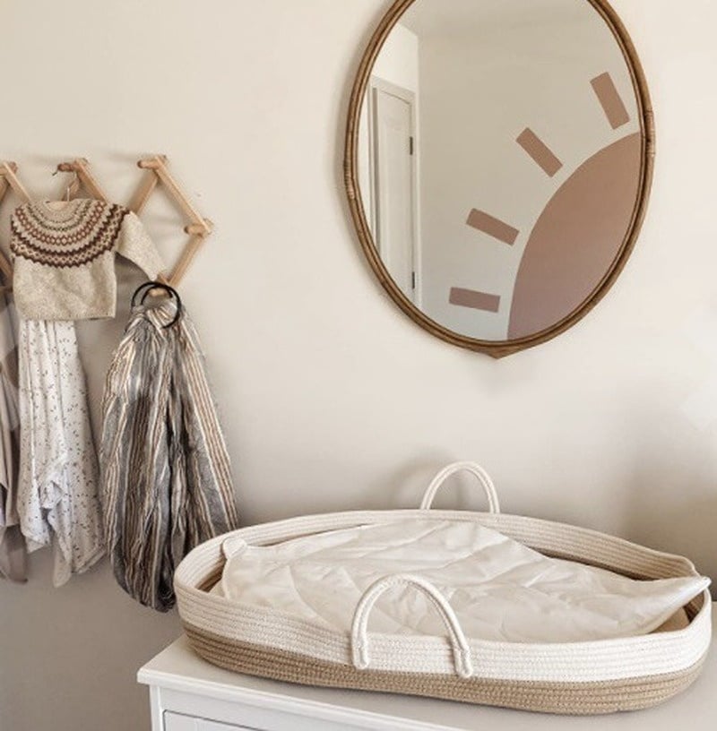 Couffin en rotin blanc et marron posé sur une étagère banche. On voit un miroir accroché au mur ainsi qu'un porte-manteau.