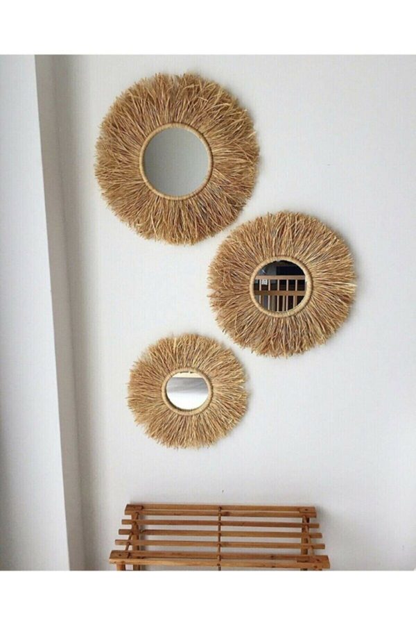 Ensemble de trois miroirs ronds en forme de soleil, en raphia. Tons naturels, ils sont accrochés à un mur blanc.