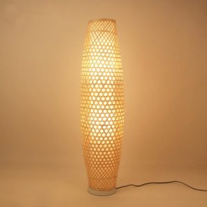 Ce lampadaire est en rotin , il a une forme ovale et est entouré de murs beiges.