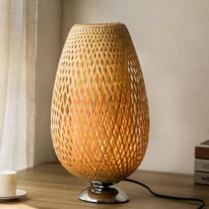 Cette lampe de chevet est ovale et avec un pied en métal. Elle est posée sur une table en bois.