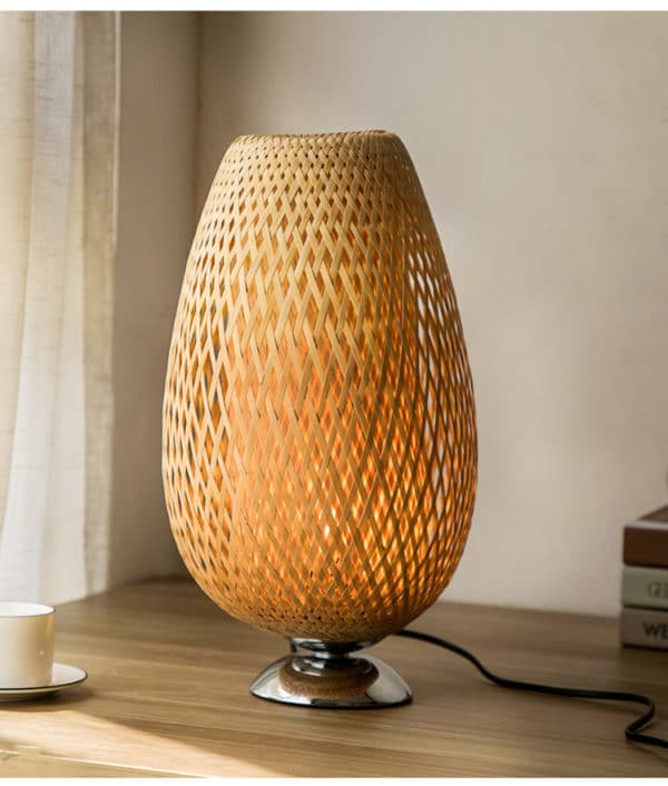 Cette lampe de chevet est ovale et avec un pied en métal. Elle est posée sur une table en bois.