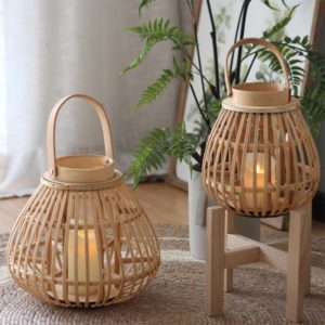 Magnifique lanterne en rotin, bambou, matière durable, aspect minimaliste et naturel . Il y a une anse. La lanterne est posée sur un tabouret, dans une très belle pièce décorée avec soin. Une autre lanterne plus grosse est posée près d'elle.
