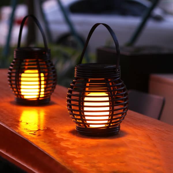 Lanternes d'extérieur, solaires, avec une anse. Elles sont posées sur une table d'extérieur.