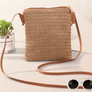 Joli sac en paille et rotin avec une grande lanière en bandoulière en simili cuir. Il est posé sur une table près de lunettes de soleil et d'une plante.
