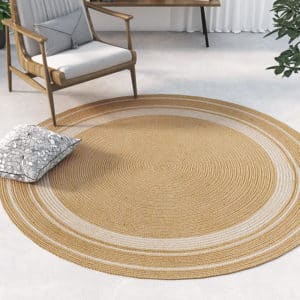 Magnifique tapis rond en jute avec trois cercles blancs aux extrémités. Il est positionné dans une pièce contemporaine et lumineuse au pied d'un fauteuil.