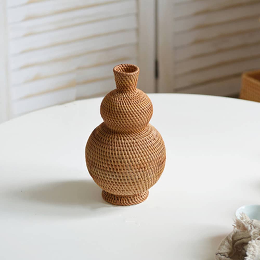 Très beau vase tissé en rotin formé de deux sphères. Harmonieux. Il est posé sur une table blanche.