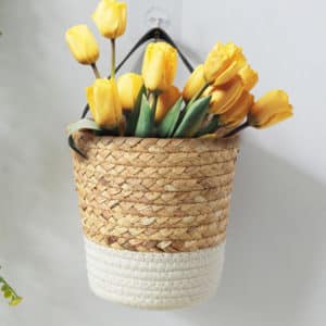 Vase en rotin couleur blanche et naturelle, suspendu au mur blanc, avec des tulipes jaunes