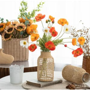Joli vase en verre et en rotin sur une table entouré d'autres vases en rotin. Il accueille un bouquet de fleurs des champs.