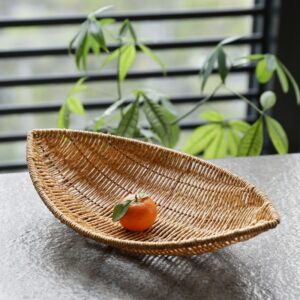 panière à fruits en matière naturelle tissée, en forme de feuille avec une clémentine au centre, elle est posée sur un plan de travail devant une fenêtre et une plante verte