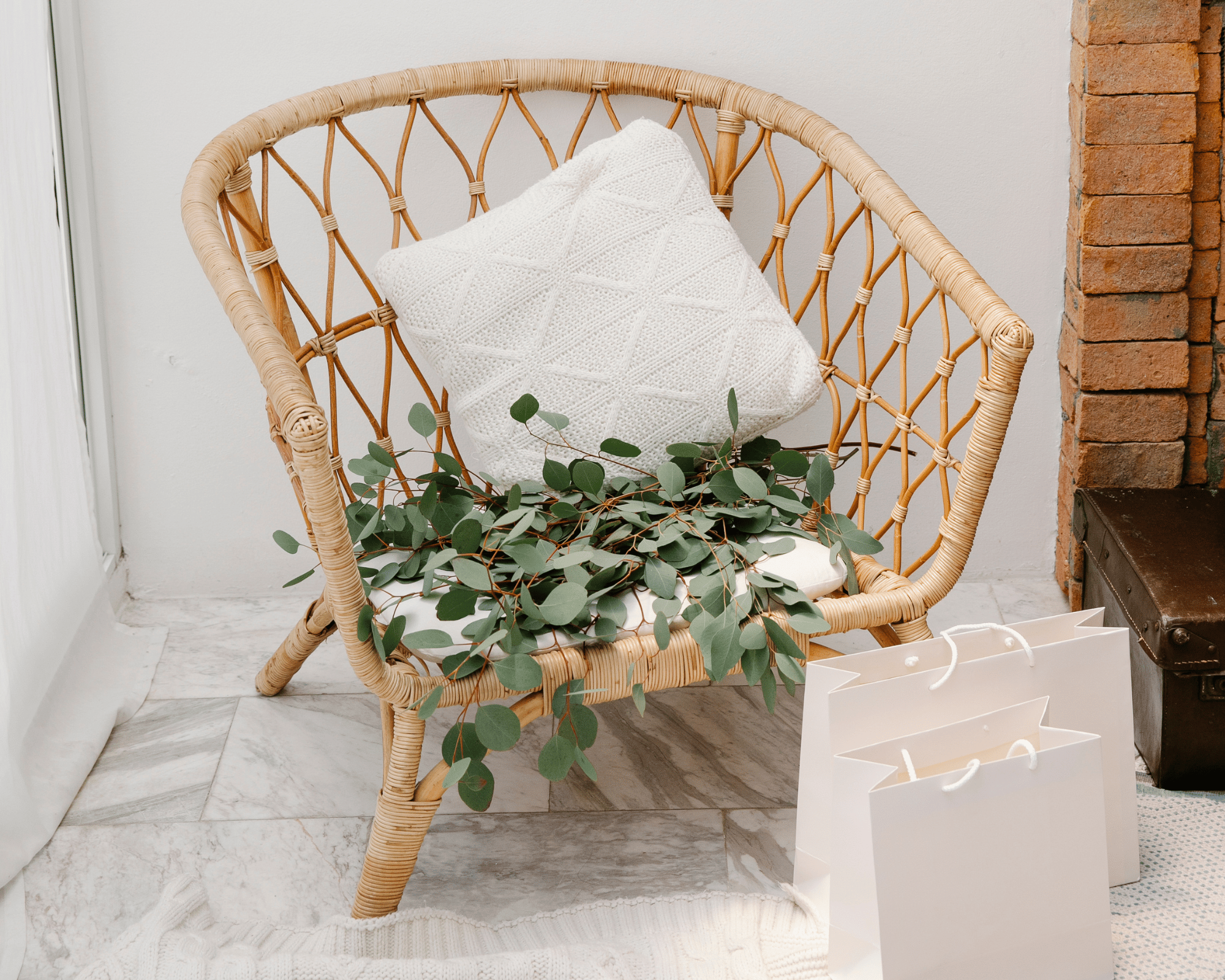 Fauteuil en rotin avec un coussin blanc et des petites feuilles de lierre en décoration , près du fauteuil deux sachet de shopping balncs