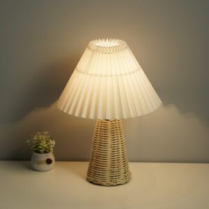 Posée sur une table , une lampe avec la base en forme de cône en rotin, et l'abat-jour plissé blanc