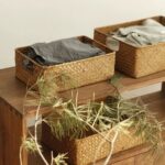 3 paniers de rangement remplis de linge plié, posé sur un meuble en bois, avec une plante posée dessus