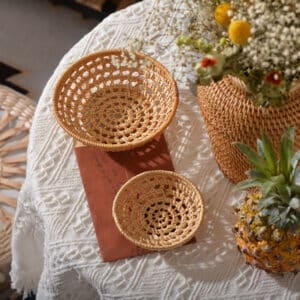 deux petits paniers de tables en rotin posés sur une table avec une nappe blanche près de pots de fleurs