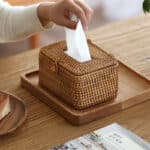 Boîte à mouchoirs en bambou tissée à la main pour la maison, avec mouchoir blanc à l'intérieur avec une main qui récupère un mouchoire