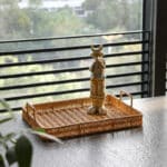 Plateau de rangement en plastique imitation rotin marron avec poignée de chaque côté, sur un table avec une statuette dedans