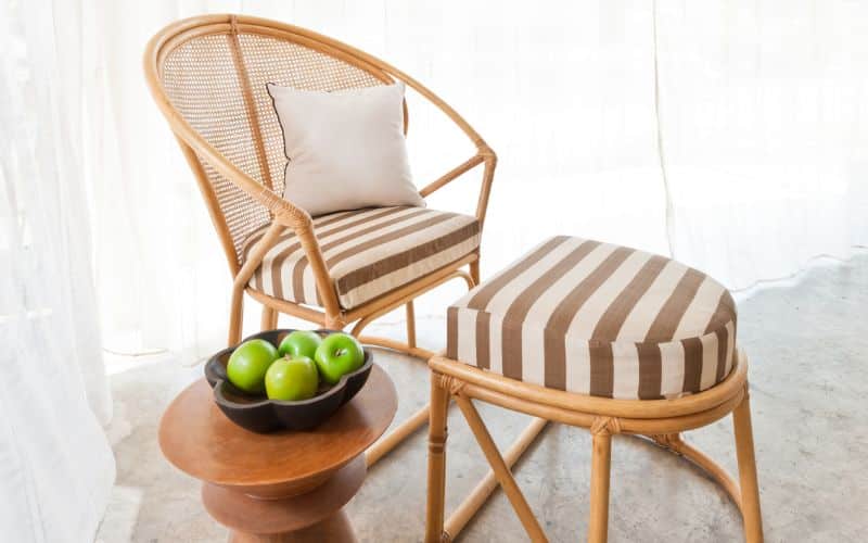 fauteuil en rotin avec repose pied et un table d'appoint avec une corbeille de pomme verte dessus