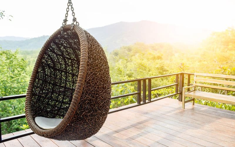 Terrasse avec vu sur la nature, où est accroché un fauteuil en rotin, en forme d'œuf. Il est suspendu.