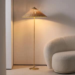 Lampadaire Effet Osier sur Pied et Minimaliste posé à côté d'un canapé gris devant un mur blanc