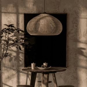 Lustre Effet Paille Tissé au Design Japonais avec une table en bois en dessous une plante verte à gauche et un tableau noir en fond