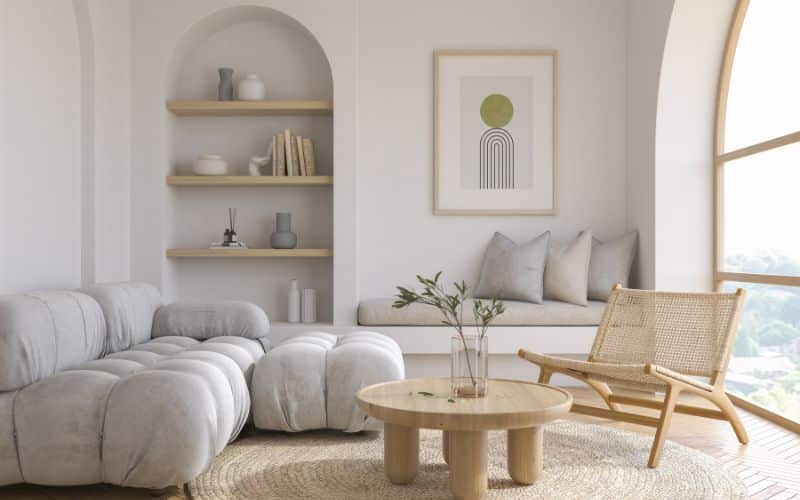 Salon très moderne avec un canapé d'angle gris très clair, une table basse ronde en bois claire, un fauteuil moderne en rotin, un cadre moderne accroché au mur.