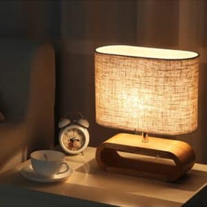 Lampe de Chevet Chic et Élégante allumée et posée sur une table de nuit avec petit réveil à côté